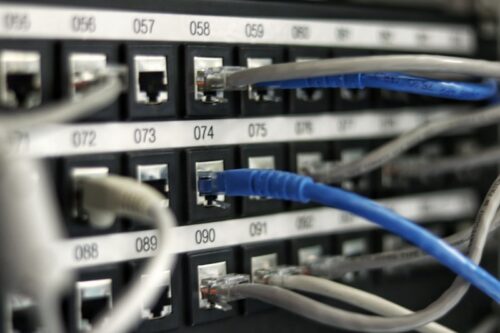A network patch panel with blue and grey ethernet cables connected to numbered ports
